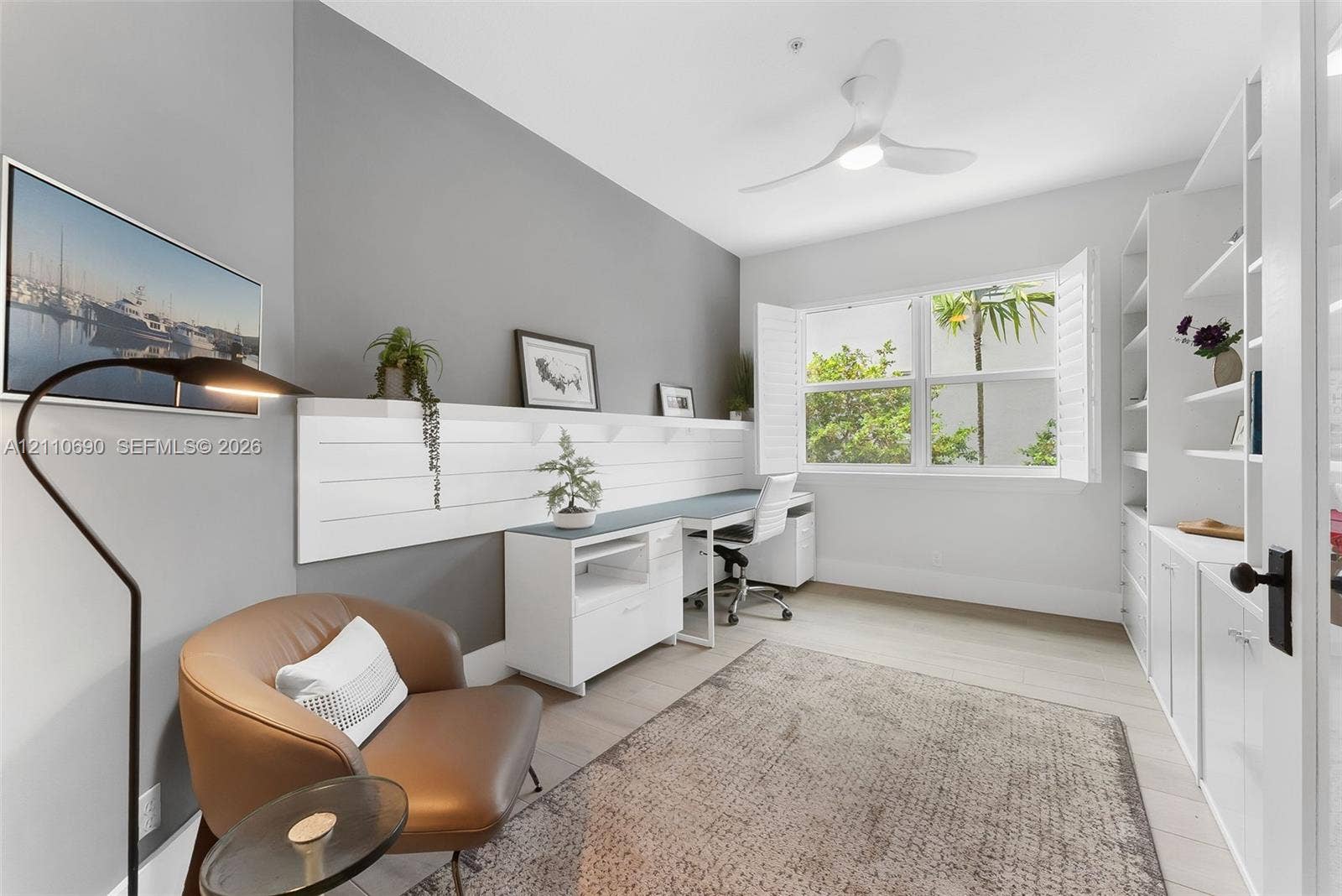 Built-in white shelving, wood-finish flooring, white plantation shutters, three-blade ceiling fan with integrated light, and white shiplap accent wall