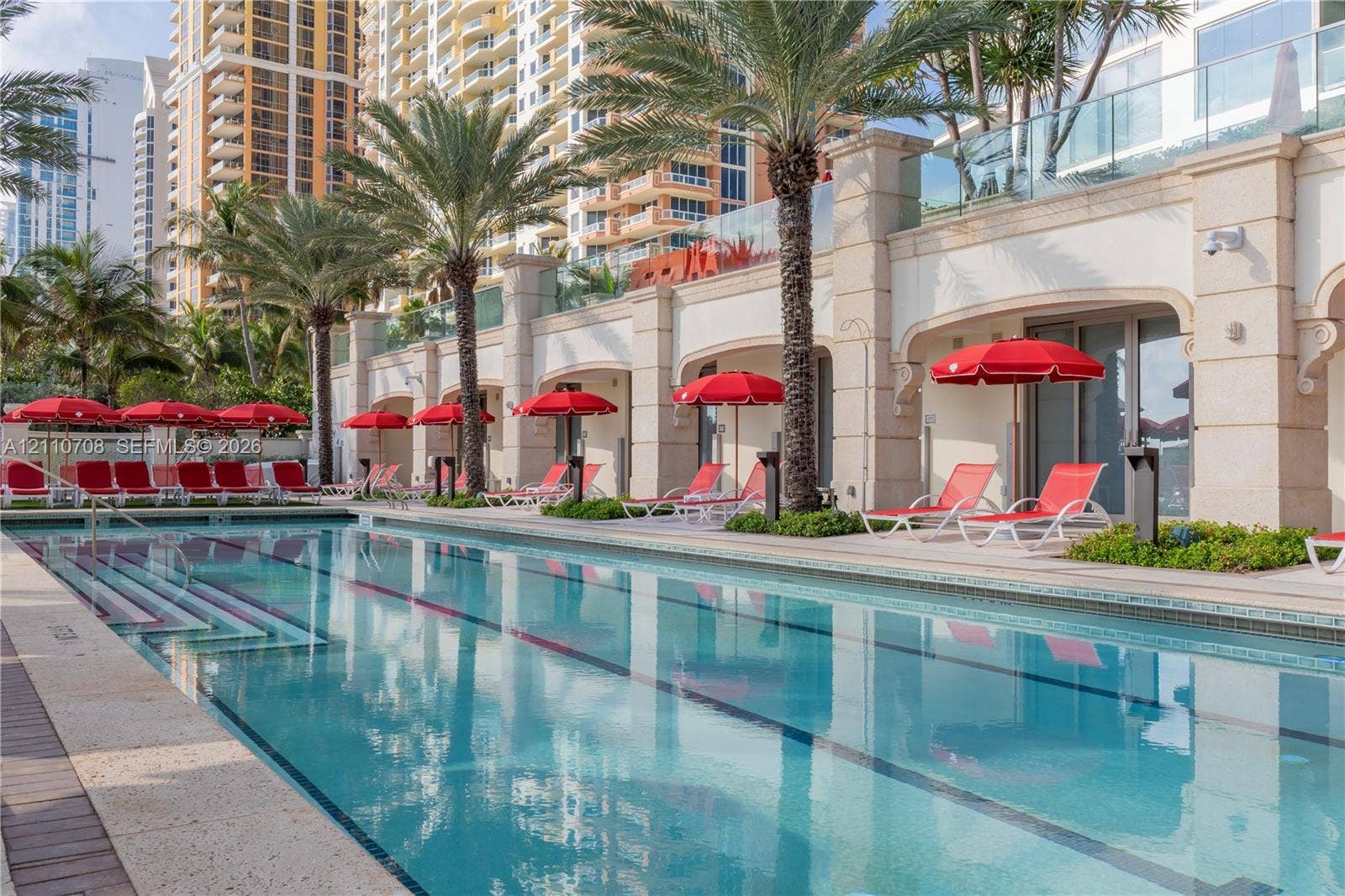 Lap pool featuring light-colored stone decking, glass panel railings, and masonry exterior detailing with arched recessed openings
