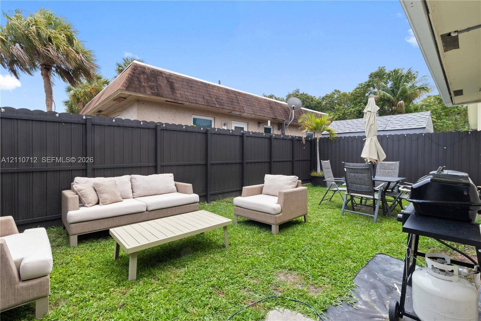 Private backyard enclosed by dark-toned metal fencing with a level lawn and mature palm trees