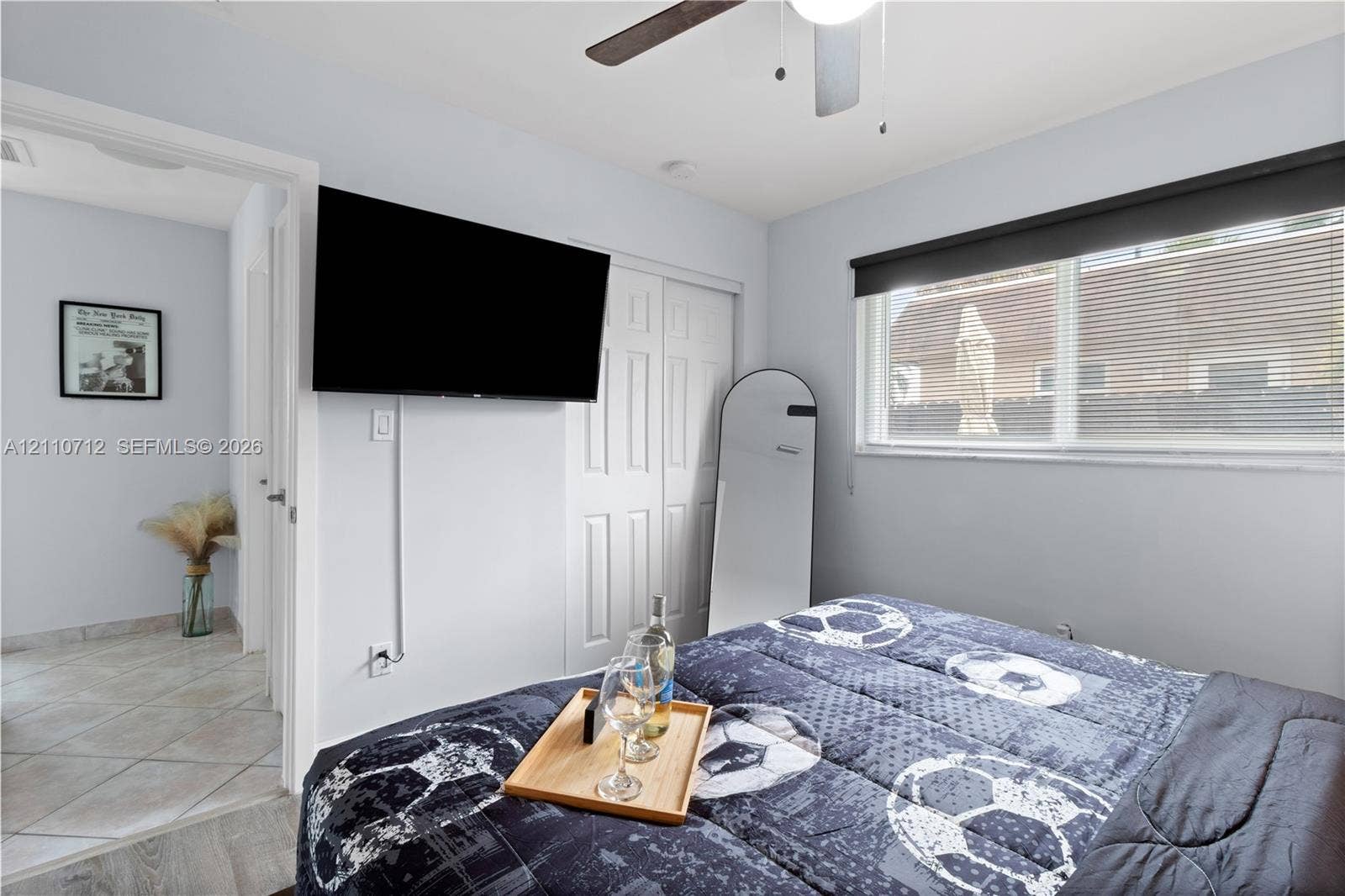 Bedroom featuring light-toned interior walls, dual-panel closet doors, ceiling fan with integrated lighting, and a window with a blackout roller shade