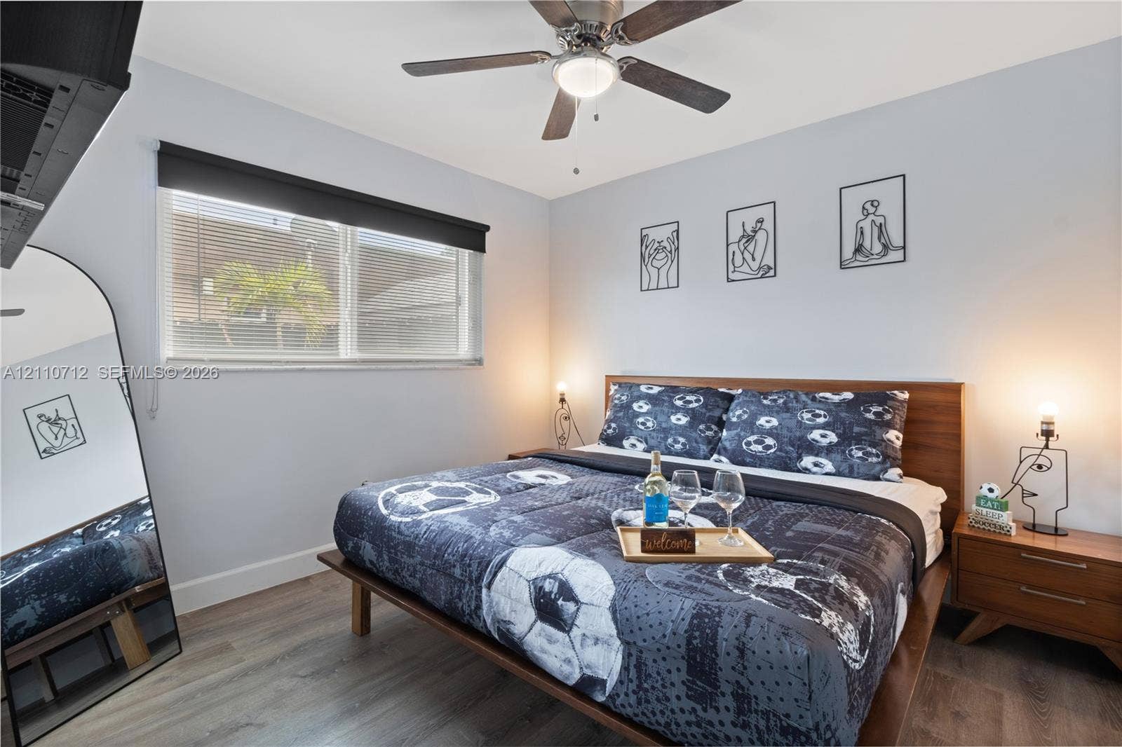 Bedroom featuring wood-finish flooring, a ceiling fan with integrated lighting, and a window with a roller shade