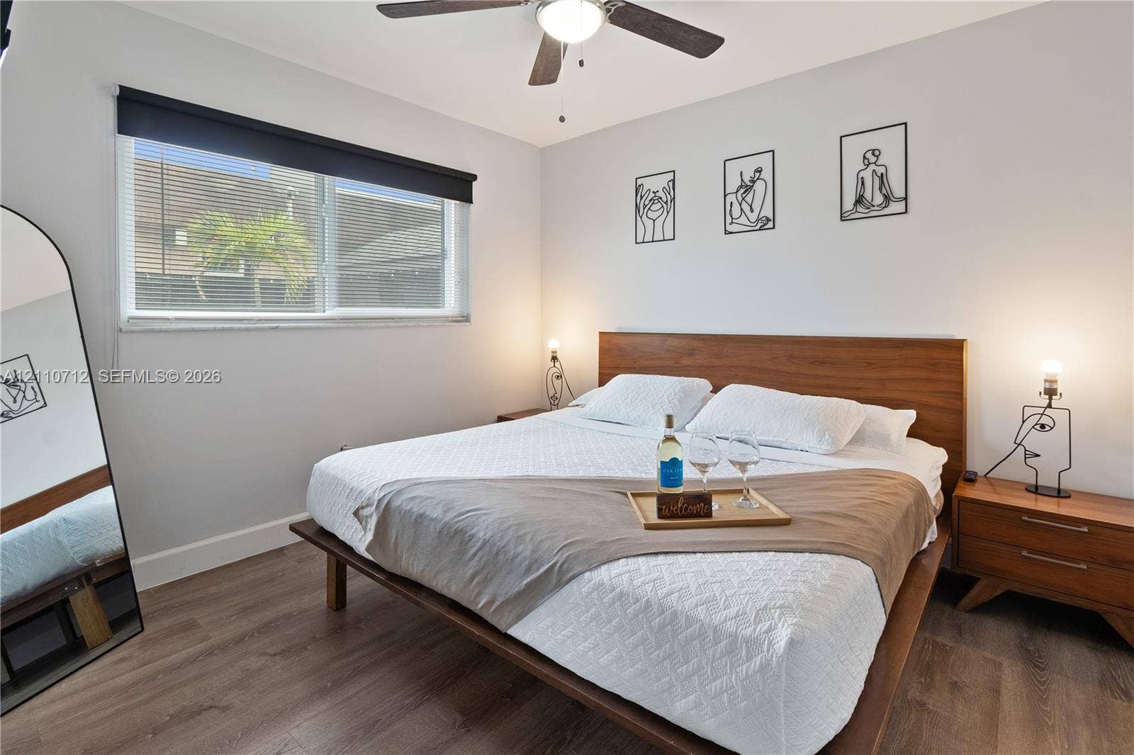 Room featuring wood-finish flooring, a ceiling fan with integrated lighting, and a window with a retractable shade