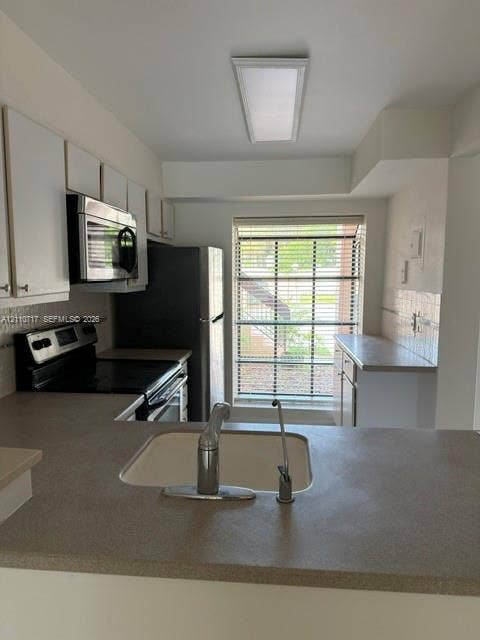 2297 SW 15th Street, #125, Deerfield Beach, Deerfield Beach, FL 33442 Kitchen featuring flat-panel white cabinetry, solid-surface countertops, integrated stainless steel appliances, and a rectangular window with horizontal blinds