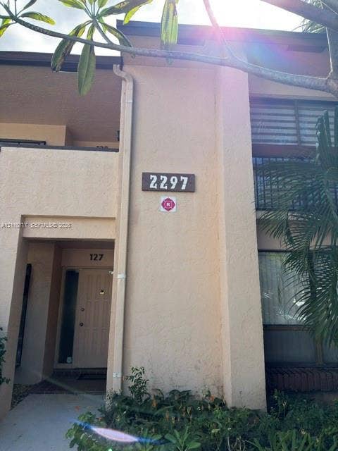 2297 SW 15th Street, #125, Deerfield Beach, Deerfield Beach, FL 33442 Stucco exterior facade featuring a covered entryway, private balcony with horizontal railings, and integrated address plaque