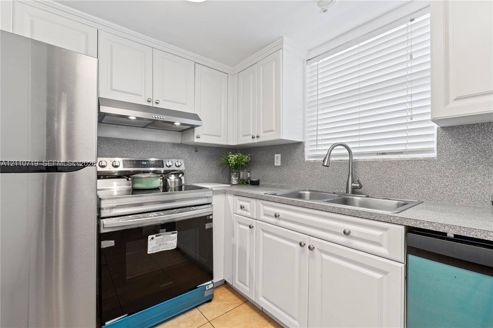 9375 Fontainebleau Boulevard, #L314, Miami, FL 33172 Kitchen featuring white shaker-style cabinetry, stainless steel appliances, speckled stone-finish countertops, dual-basin under-mount sink with pull-down faucet, and neutral tile flooring