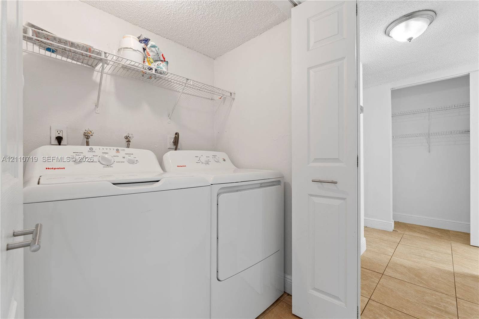 9375 Fontainebleau Boulevard, #L314, Miami, FL 33172 Laundry area featuring tile flooring, white bi-fold door, and wire shelving