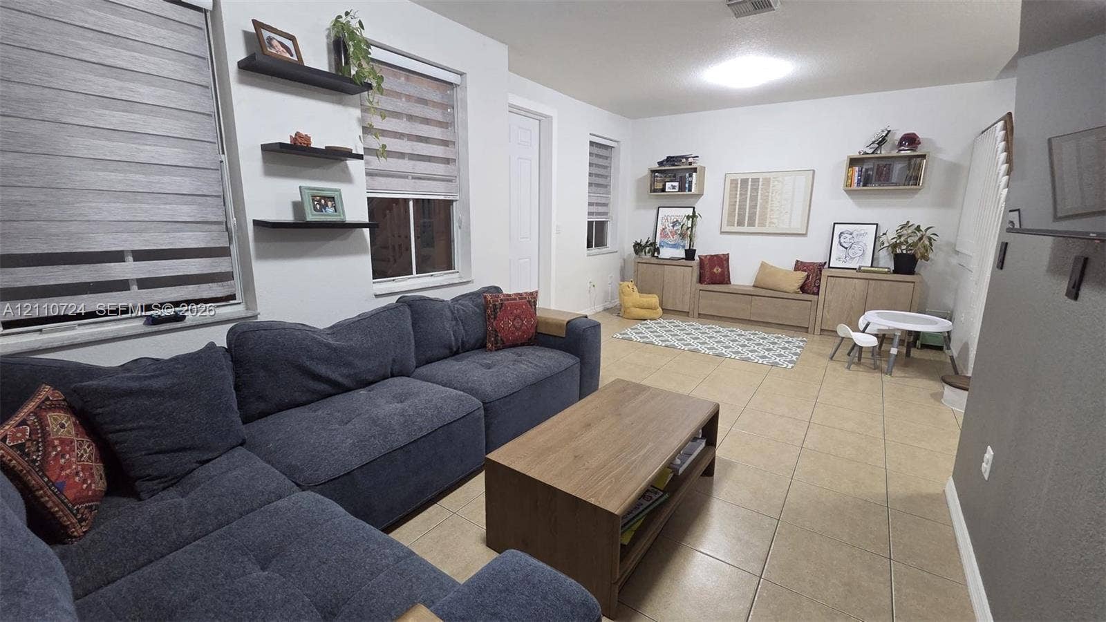 10846 SW 240th Lane, Homestead, FL 33032 Living space featuring large-format tile flooring, built-in cabinetry, floating wall shelves, and dual-layered window treatments