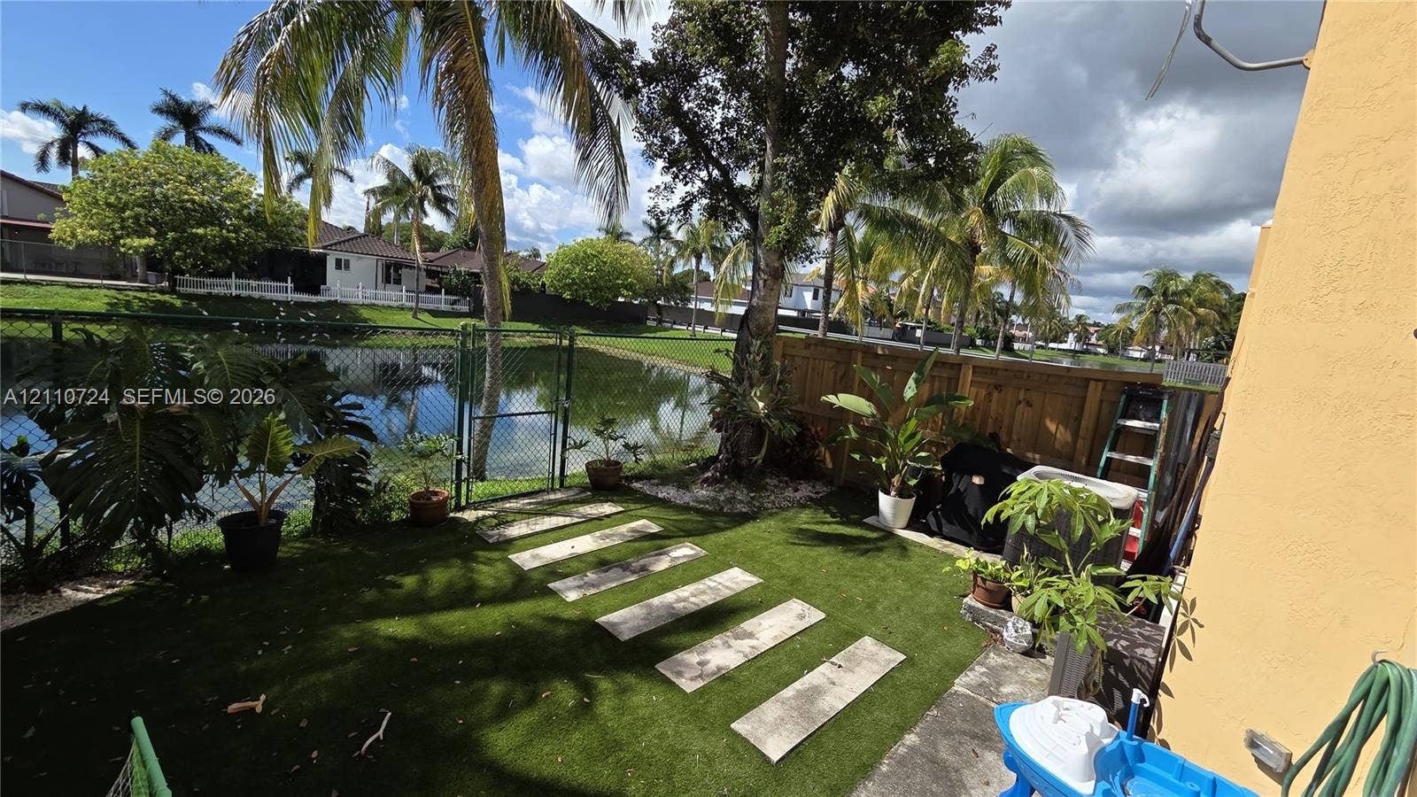 10846 SW 240th Lane, Homestead, FL 33032 Rear patio featuring artificial turf, concrete stepping stones, a wood privacy fence, and a chain-link gate leading to the waterfront