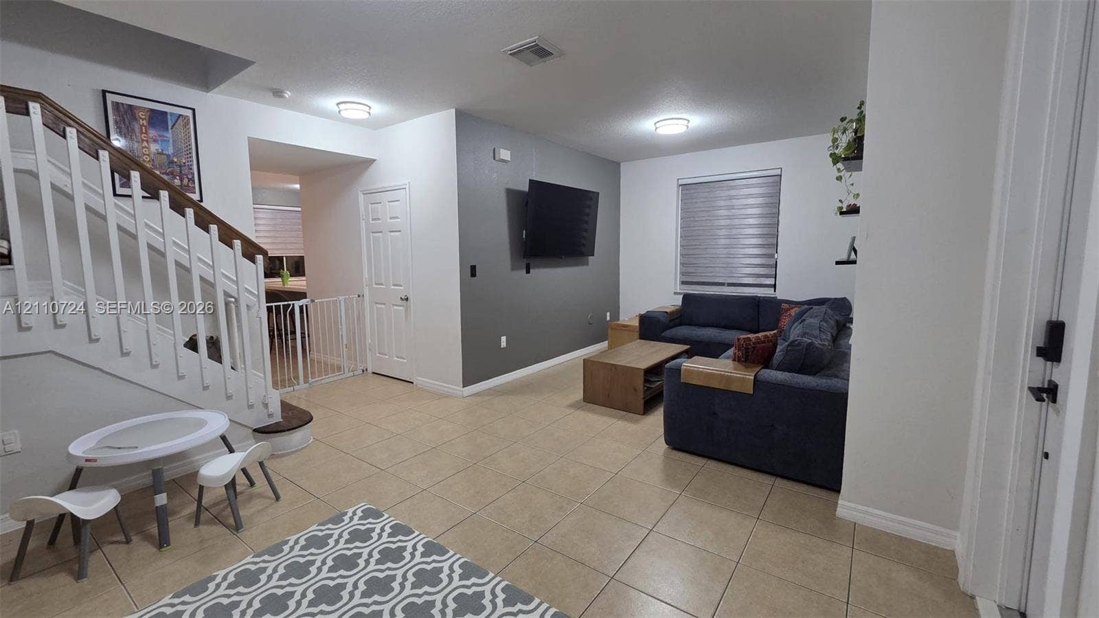 10846 SW 240th Lane, Homestead, FL 33032 Open-concept interior featuring large-format tile flooring, a staircase with a wooden handrail, and a charcoal accent wall