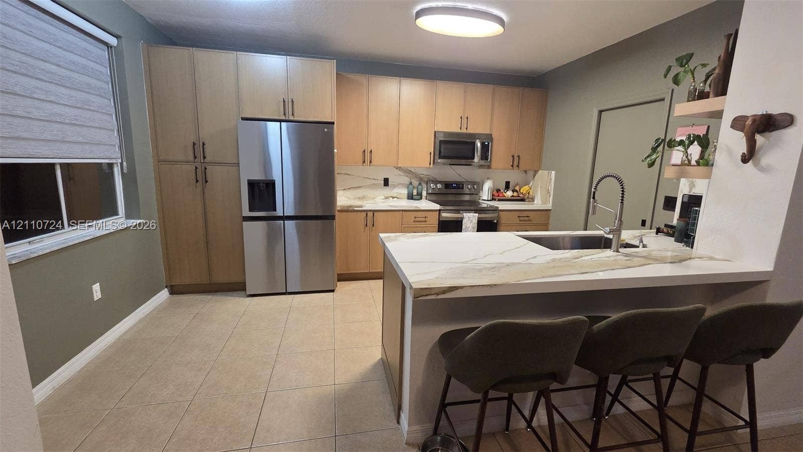 10846 SW 240th Lane, Homestead, FL 33032 Kitchen featuring flat-panel wood-finish cabinetry, stone-surface countertops with waterfall edge, stainless steel refrigerator, undermount sink with arched pull-down faucet, and neutral tile flooring