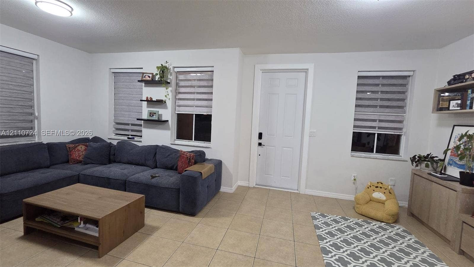 10846 SW 240th Lane, Homestead, FL 33032 Neutral-toned tile flooring, four windows featuring dual-layer roller shades, wall-mounted display shelving, and an exterior entry door