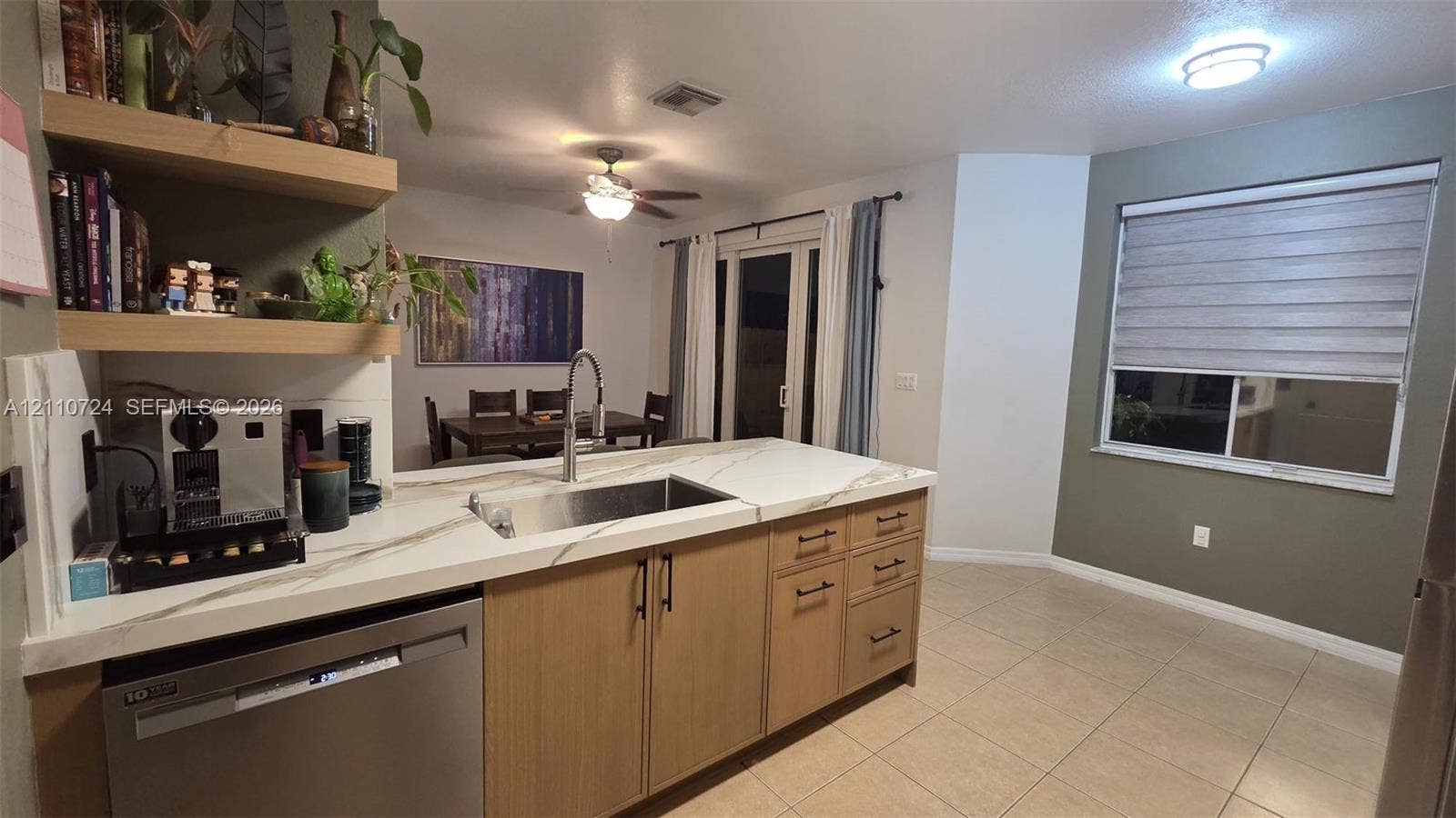 10846 SW 240th Lane, Homestead, FL 33032 Kitchen featuring a waterfall-edge countertop, stainless steel undermount sink, floating wooden shelving, light-finish cabinetry with matte black hardware, and tile flooring