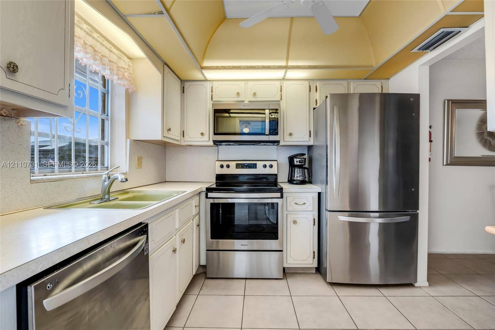 Kitchen featuring white cabinetry, stainless steel appliances, tile flooring, and a tray ceiling with integrated lighting