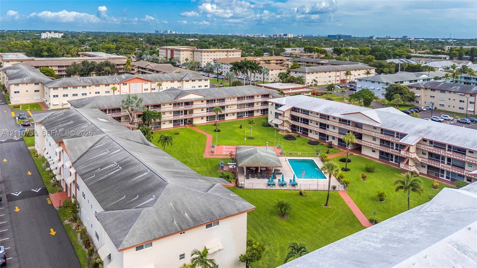 Multi-story residential complex featuring a central courtyard with a swimming pool, covered pavilion, manicured lawn, and paved walkways