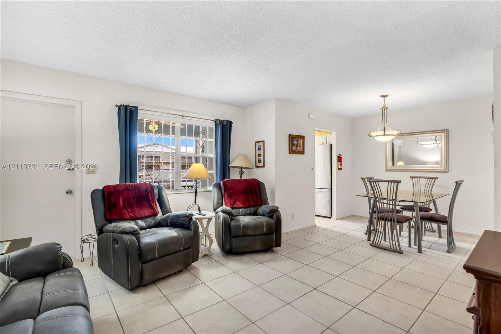 Open-concept living and dining area featuring ceramic tile flooring, multi-pane window with decorative security bars, and a multi-arm metal pendant light fixture
