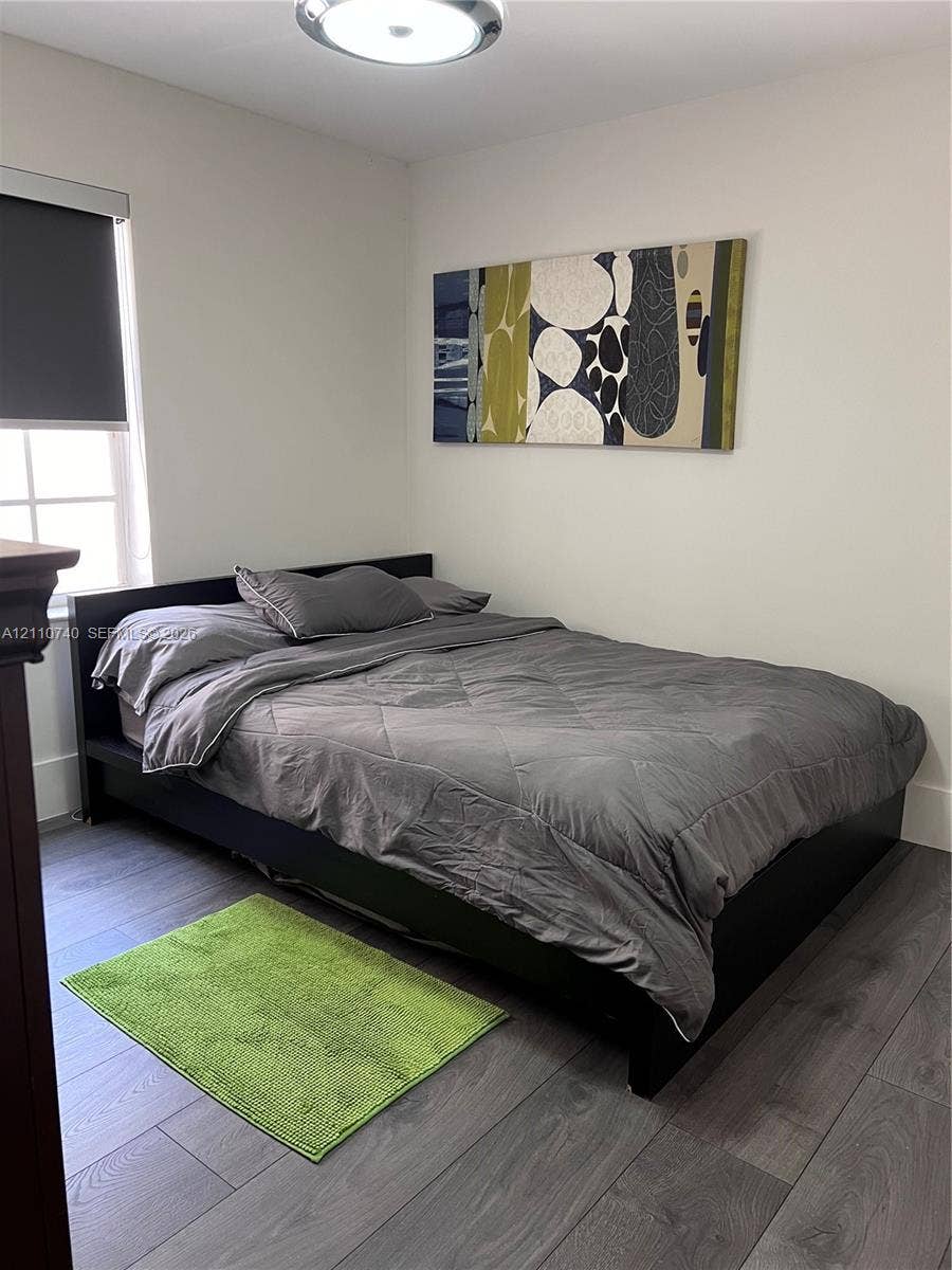 Room featuring wood-finish flooring, a multi-pane window with a roller shade, and a flush-mount overhead light fixture