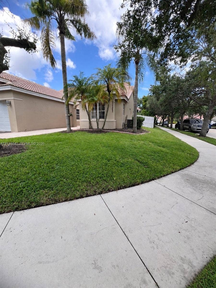 Single-story exterior featuring light-toned stucco siding, a tiled roof, mature palm trees, and a manicured lawn