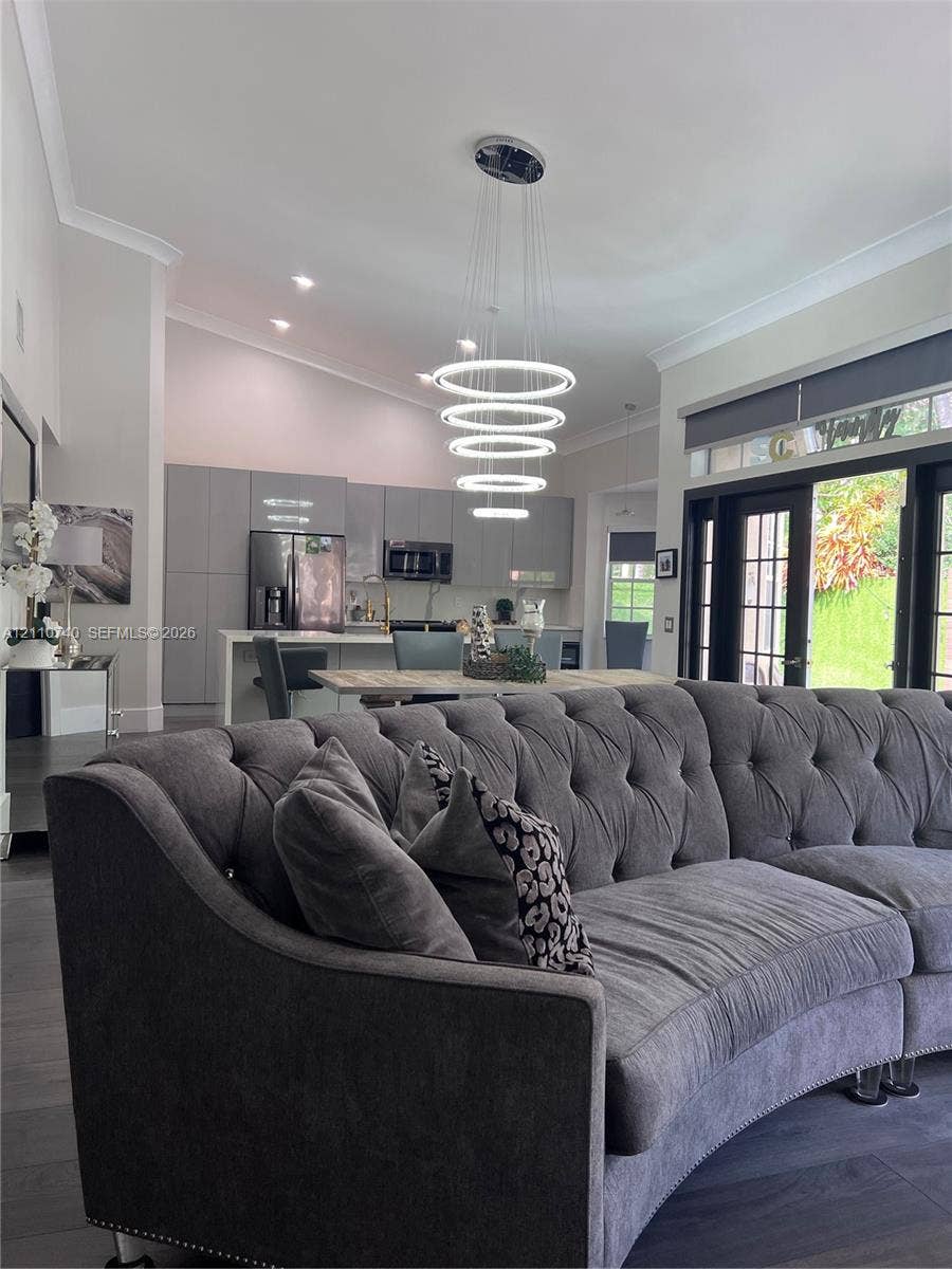 Open-concept interior featuring vaulted ceilings, modern multi-tier LED ring chandelier, dark wood-finish flooring, and floor-to-ceiling multi-panel glass doors