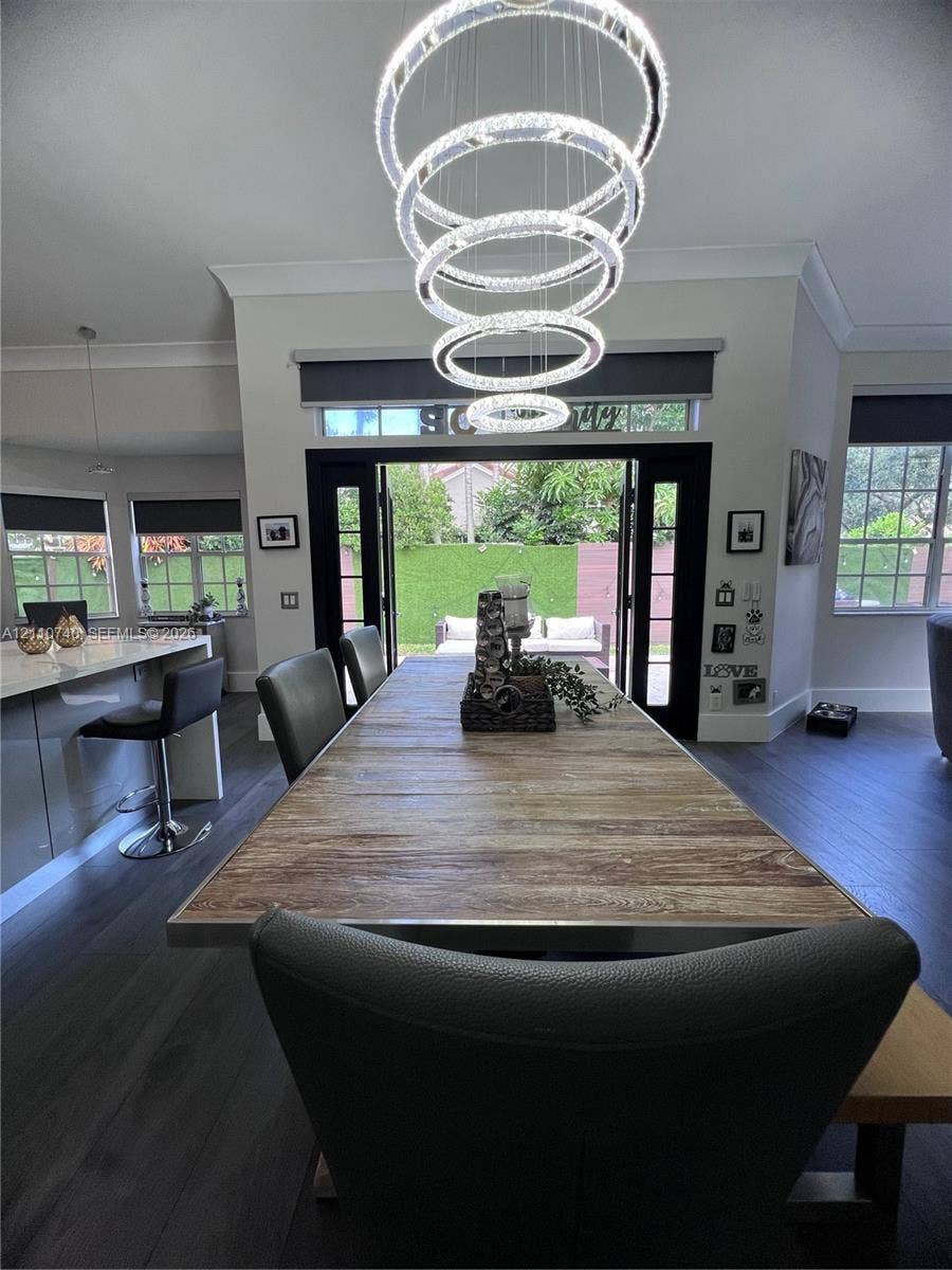 Modern multi-ring LED chandelier, dark wood-finish flooring, and black-framed French doors leading to exterior grounds