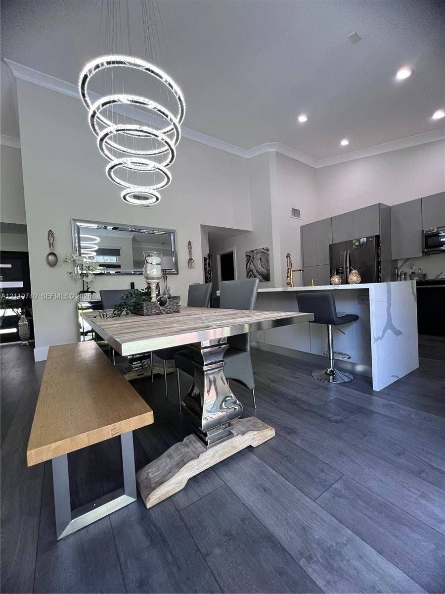 High-ceiling interior featuring wood-finish flooring, a multi-tiered circular LED pendant fixture, a waterfall-edge stone island, and flat-panel cabinetry