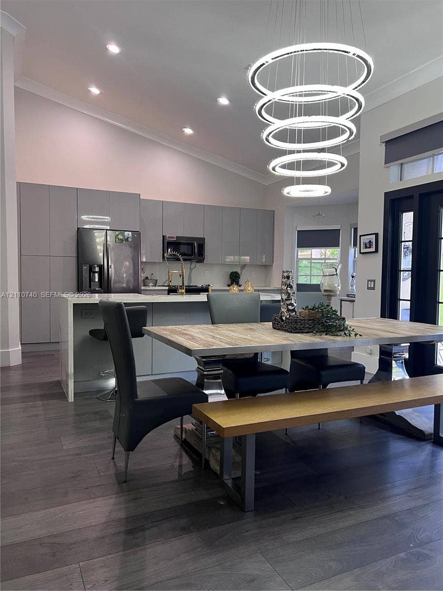 Kitchen featuring full-height flat-panel cabinetry, a stone-topped waterfall edge island, recessed ceiling lighting, a multi-tiered circular pendant fixture, and wood-finish flooring