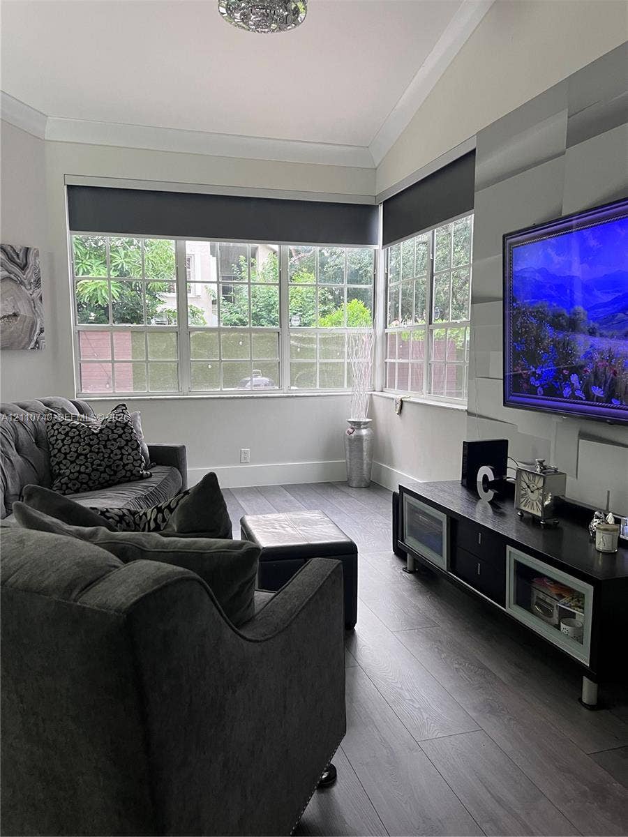 Living area featuring wood-finish flooring, vaulted ceilings with crown molding, and expansive corner windows with muntins