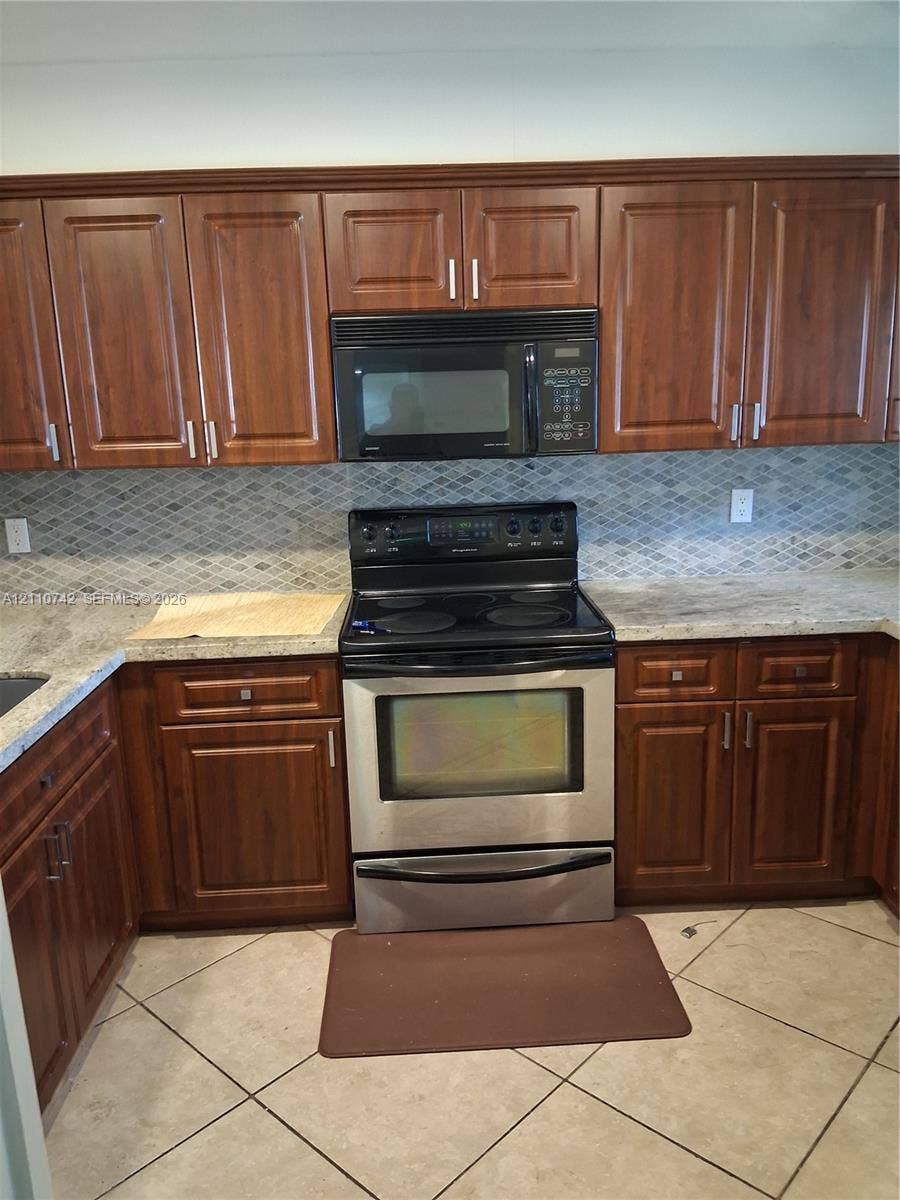 Kitchen featuring dark wood-finish cabinetry, natural stone countertops, a mosaic tile backsplash, stainless steel electric range, and an integrated built-in microwave