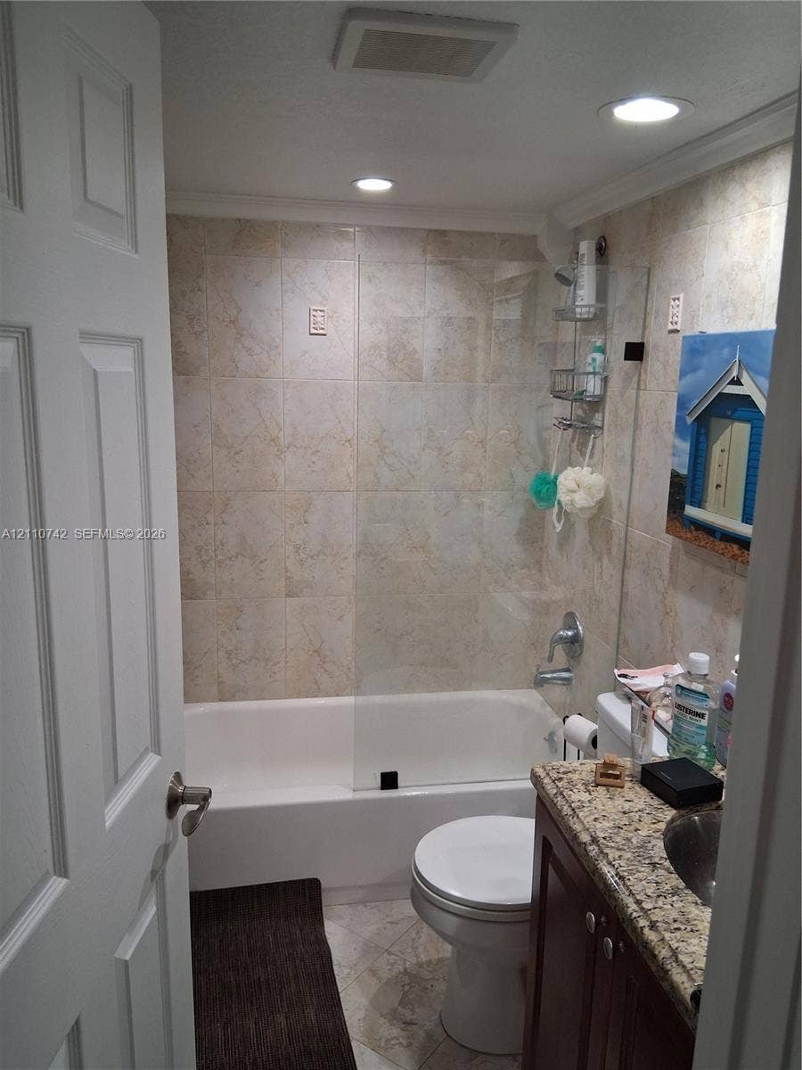 Full bathroom featuring a shower-tub combination with glass panel enclosure, tile-surround walls, stone-finish countertop, and recessed ceiling lighting