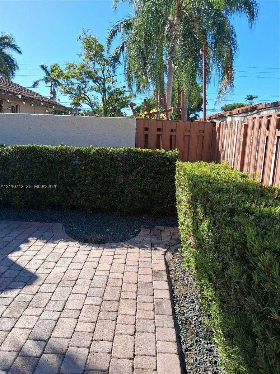 Paver patio area featuring mature hedge landscaping, a privacy fence, and gravel accents