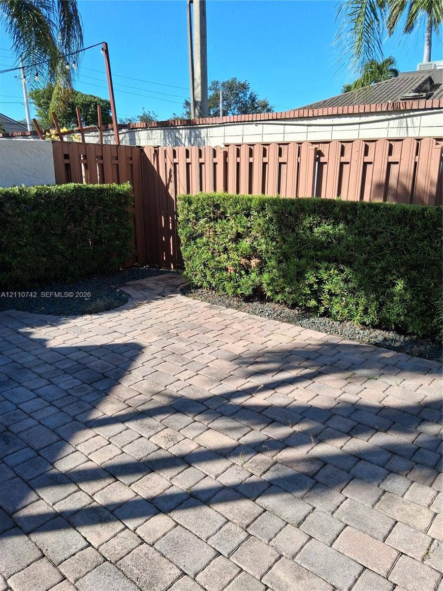 Paver patio featuring a privacy fence and manicured hedges