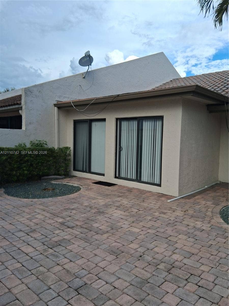 Exterior patio featuring stone paver flooring, stucco wall finish, tiled roofing, and dual sliding glass doors
