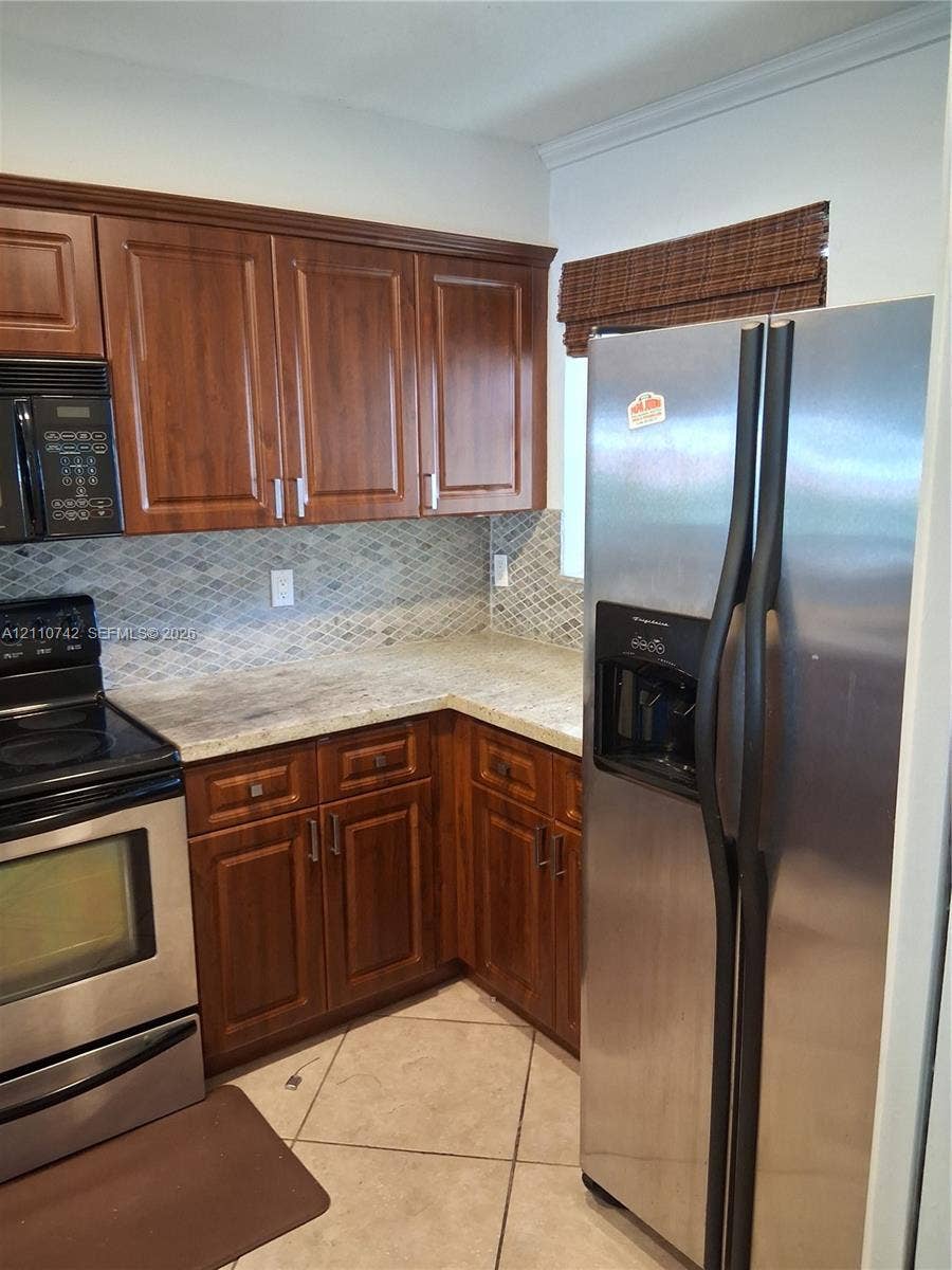 Kitchen featuring stained wood cabinetry, stone-finish countertops, geometric tile backsplash, and stainless steel appliances