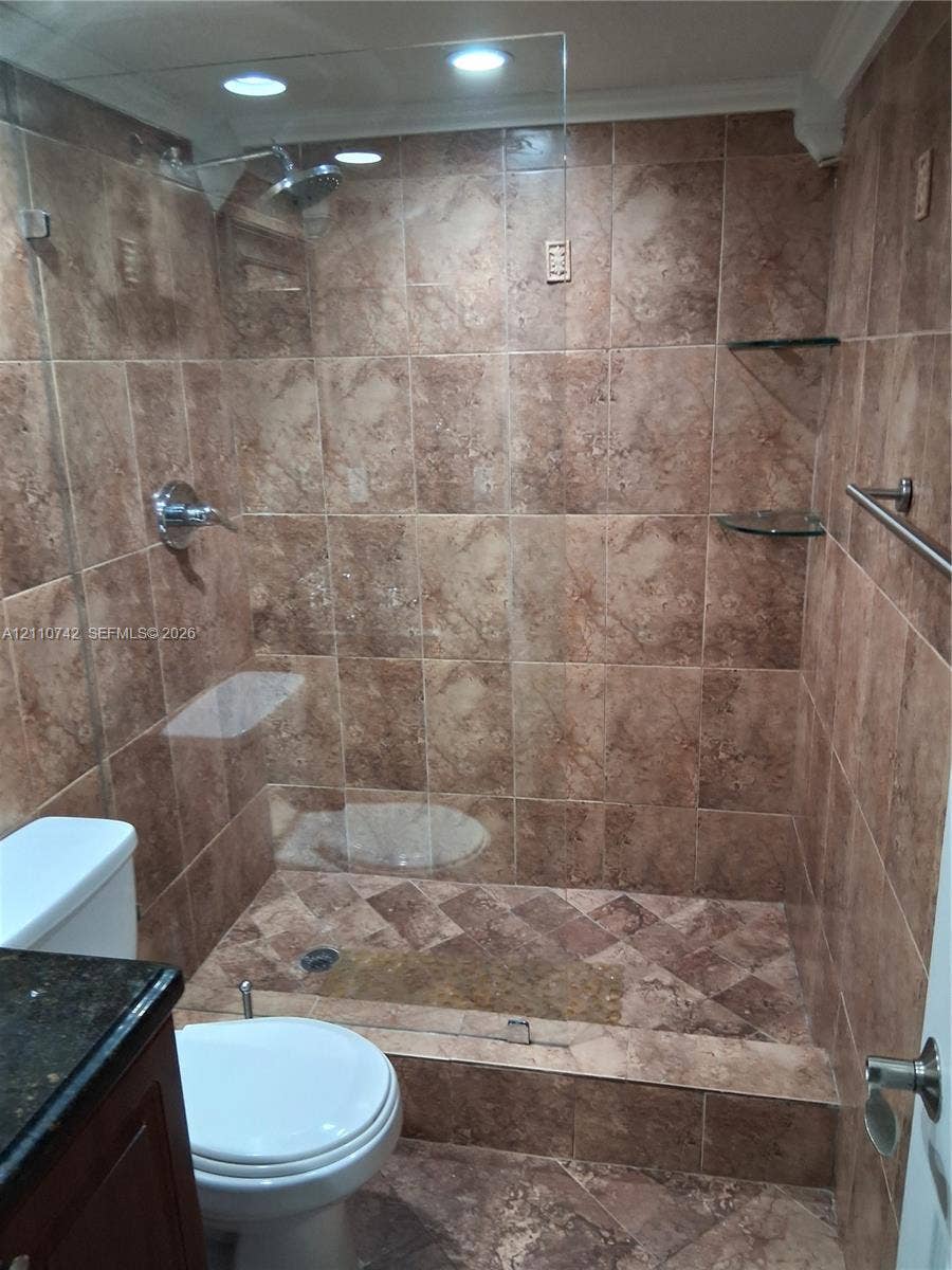 Walk-in shower featuring brown stone-finish wall and floor tile, glass panel enclosure, built-in glass shelving, and chrome-finish shower fixture