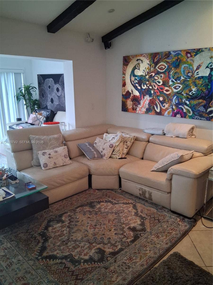 Vaulted ceiling featuring exposed dark-finish structural beams and tile flooring