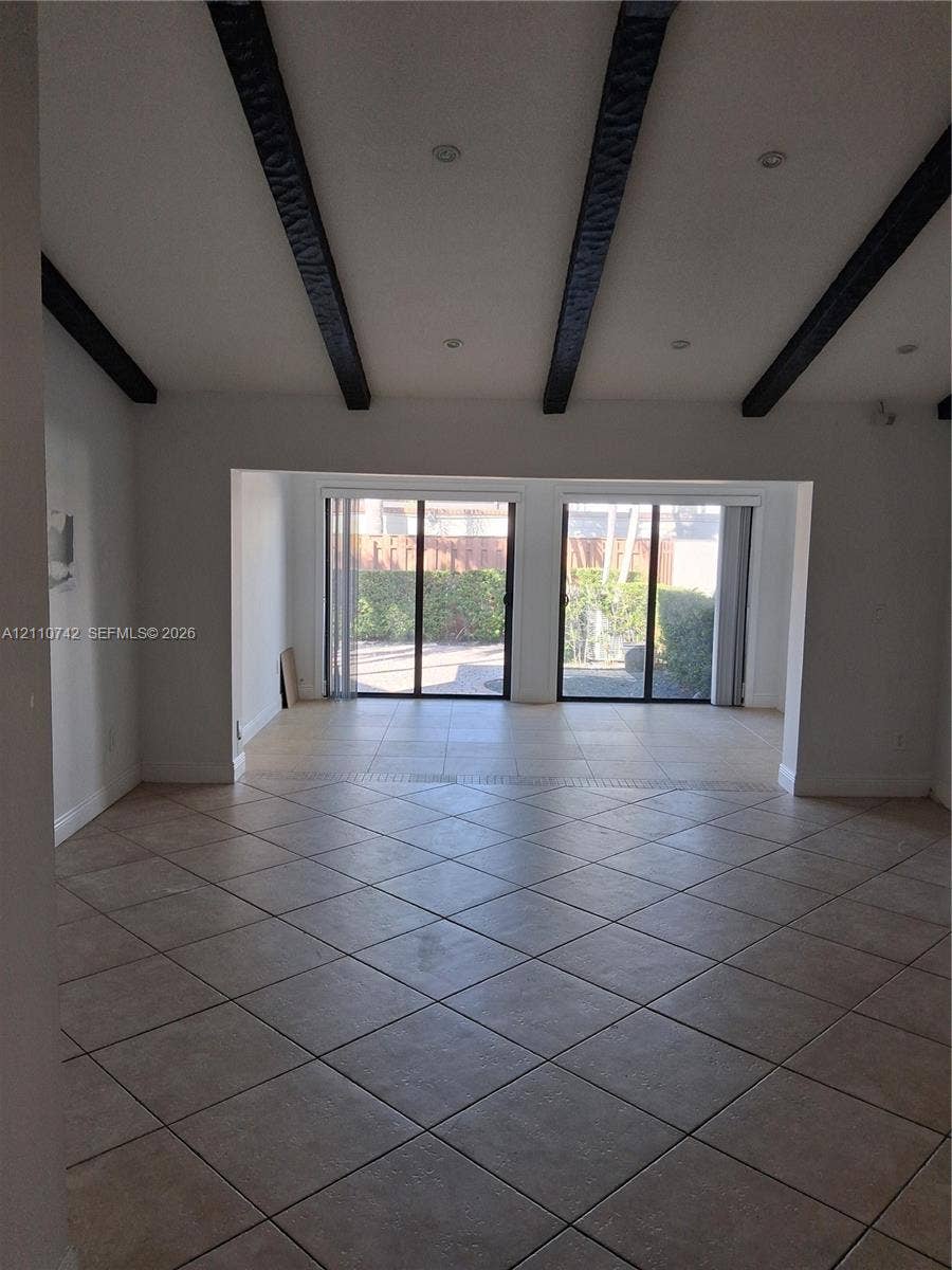 Vaulted ceilings featuring exposed dark-toned beams, recessed lighting, diagonal-set ceramic tile flooring, and dual sliding glass doors