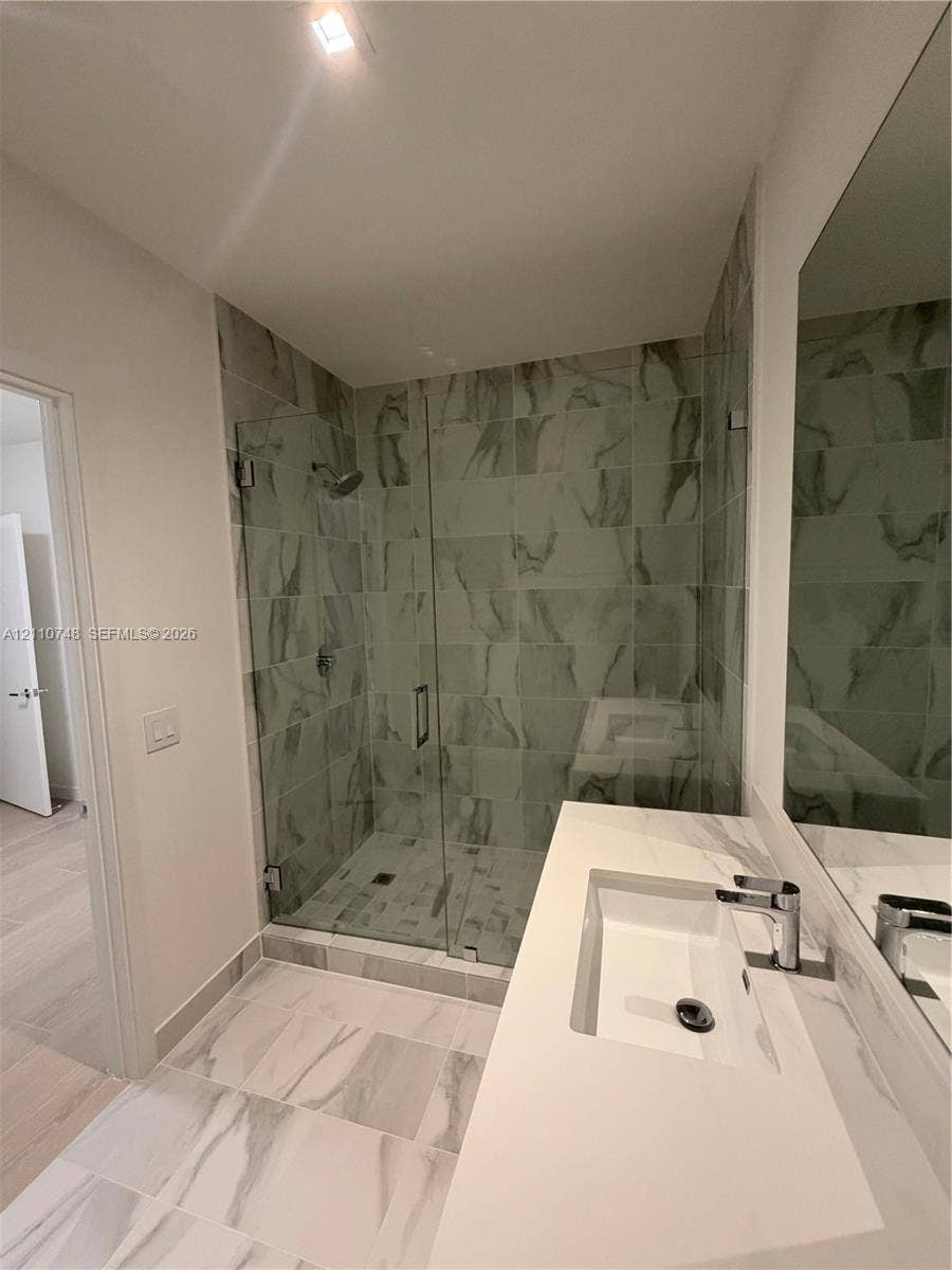Walk-in shower with floor-to-ceiling tile, frameless glass enclosure, and wall-mounted shower head, paired with a white countertop vanity featuring an integrated rectangular sink and chrome hardware