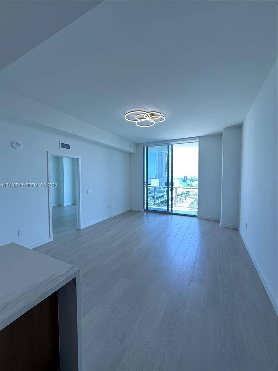 Open-concept living space featuring wood-finish flooring, floor-to-ceiling glass sliding doors, and a contemporary multi-ring LED flush-mount fixture