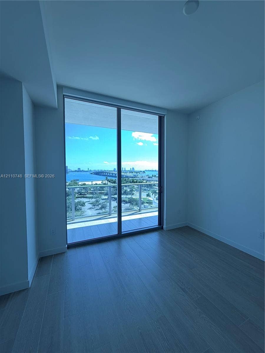 Floor-to-ceiling glass sliding doors opening to an expansive balcony, wood-finish flooring, and coastal scenery