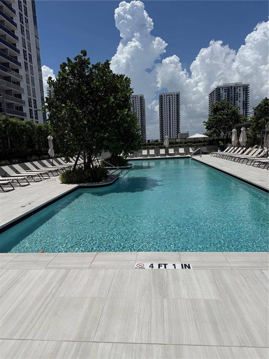Swimming pool featuring light-toned tile decking, built-in planters with mature trees, and a rectangular perimeter