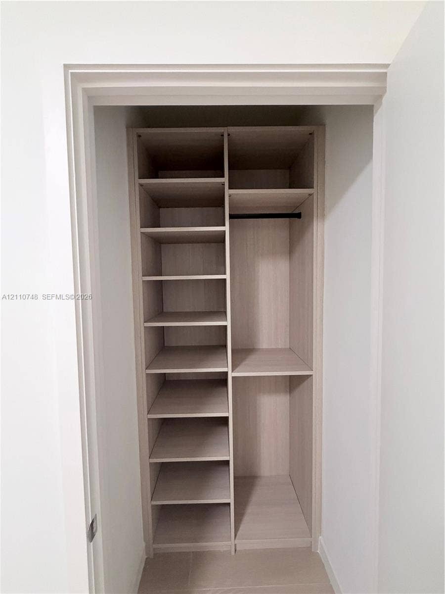 Built-in closet featuring light wood-finish shelving, multiple open storage compartments, and a horizontal hanging rod