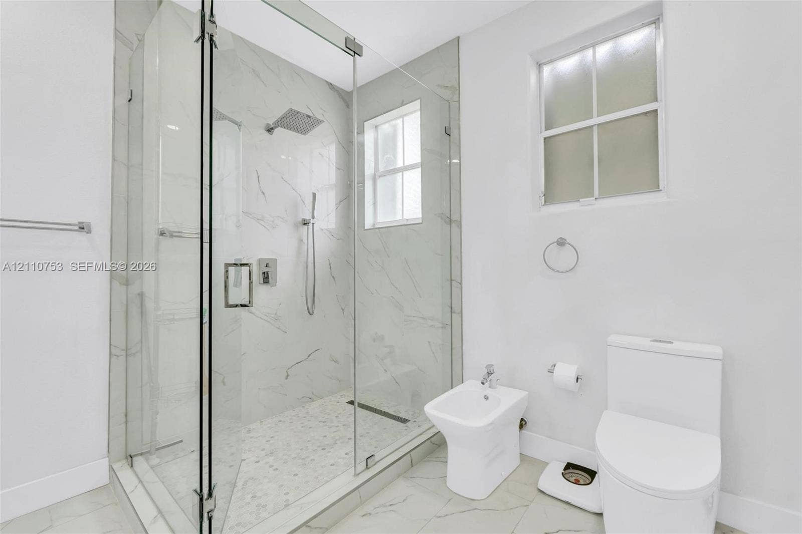 Walk-in shower with floor-to-ceiling stone-finish tile, glass enclosure, and rainfall showerhead, complemented by a bidet and dual-flush toilet