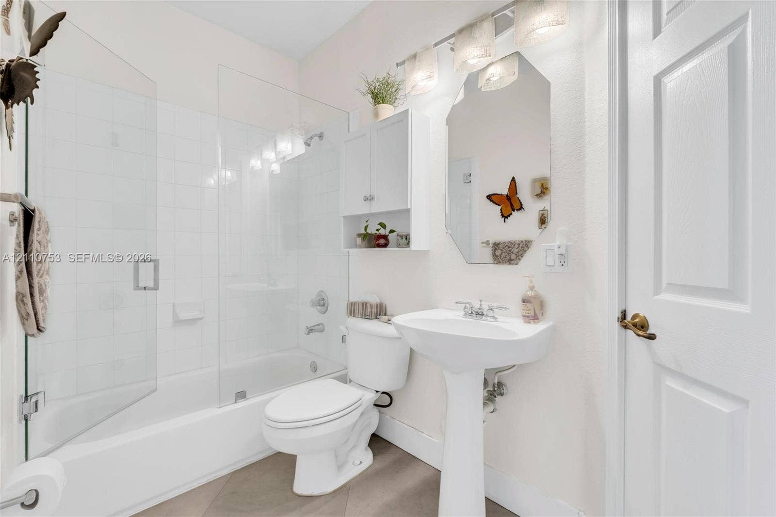 Bathroom featuring a glass-enclosed shower and tub combination, pedestal sink, wall-mounted medicine cabinet, and three-light vanity fixture