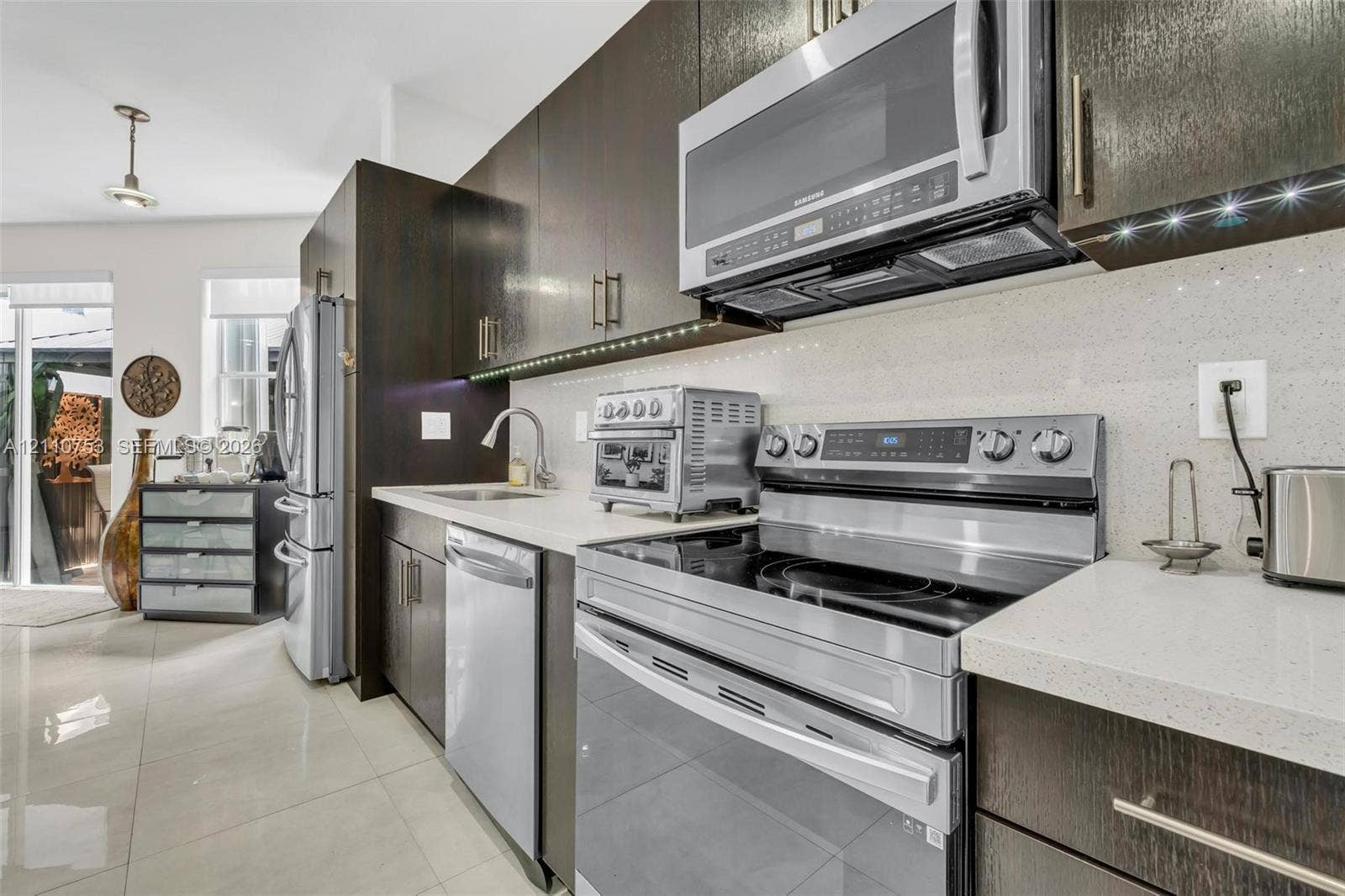 Kitchen featuring dark wood cabinetry, stainless steel appliances, light-colored quartz countertops, and polished tile flooring