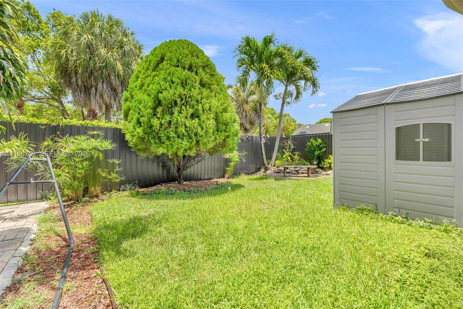 Backyard featuring a manicured lawn, privacy fencing, mature landscaping, and a detached storage structure