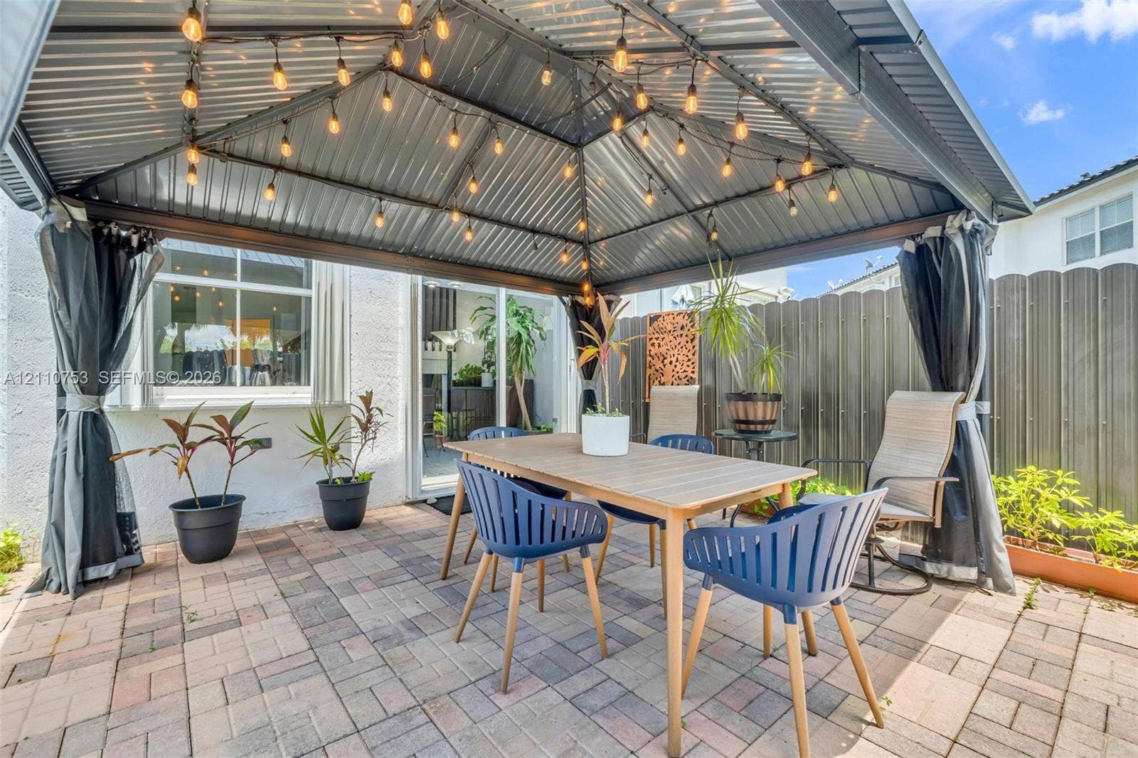 Covered patio featuring a metal gazebo structure with integrated string lighting, paver flooring, and privacy fencing