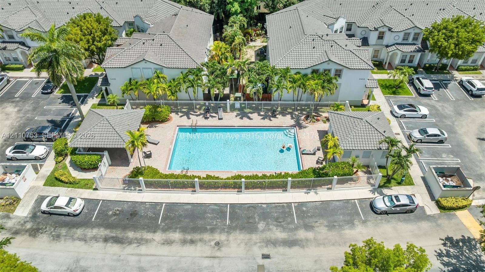 Community pool area featuring a paved deck, perimeter fencing, palm tree landscaping, and two covered gazebos