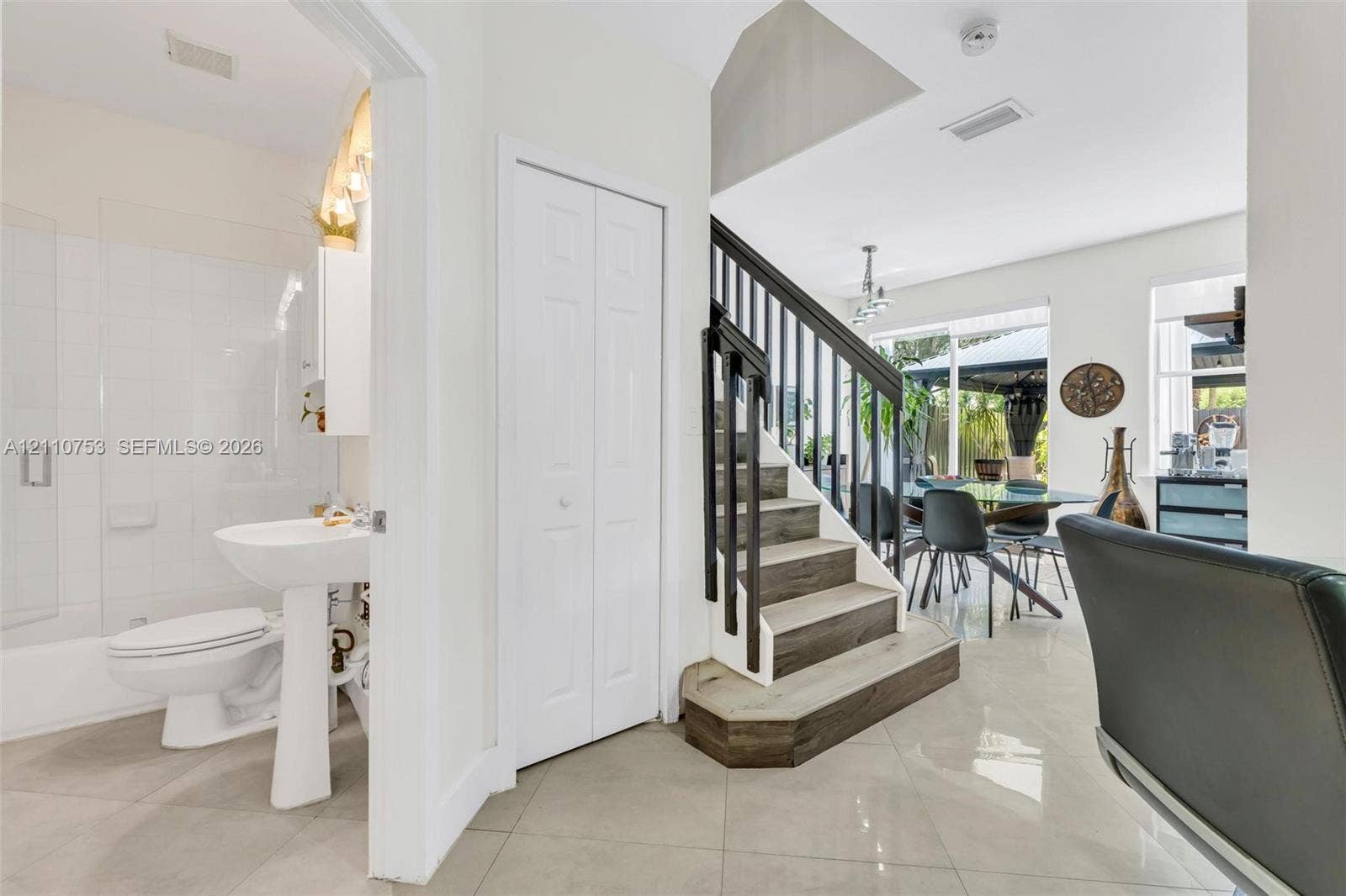 Full bathroom featuring a pedestal sink and glass-enclosed tub shower, stairs with wood-finish treads and metal balusters, and polished tile flooring throughout