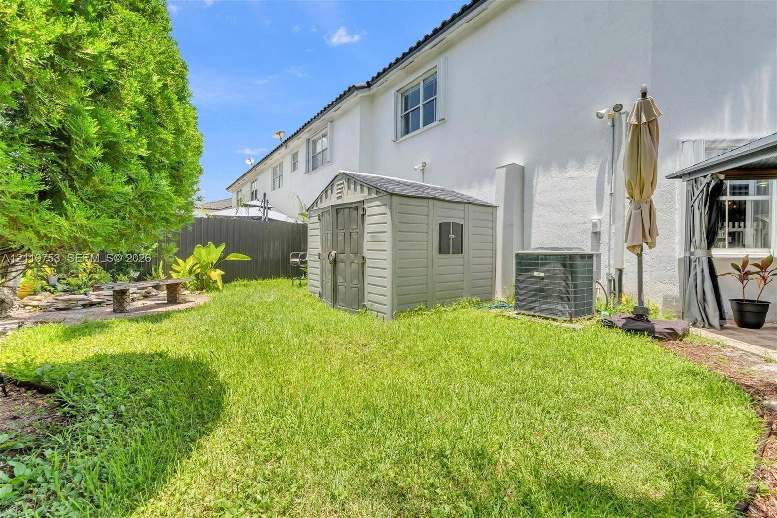 Exterior space featuring a grass lawn, paved stone area, integrated storage structure, and dark metal perimeter fencing