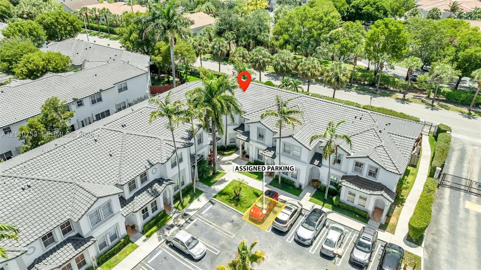 Multi-level townhouse exterior featuring a concrete tile roof, light-toned stucco facade, mature palm trees, and a designated parking space