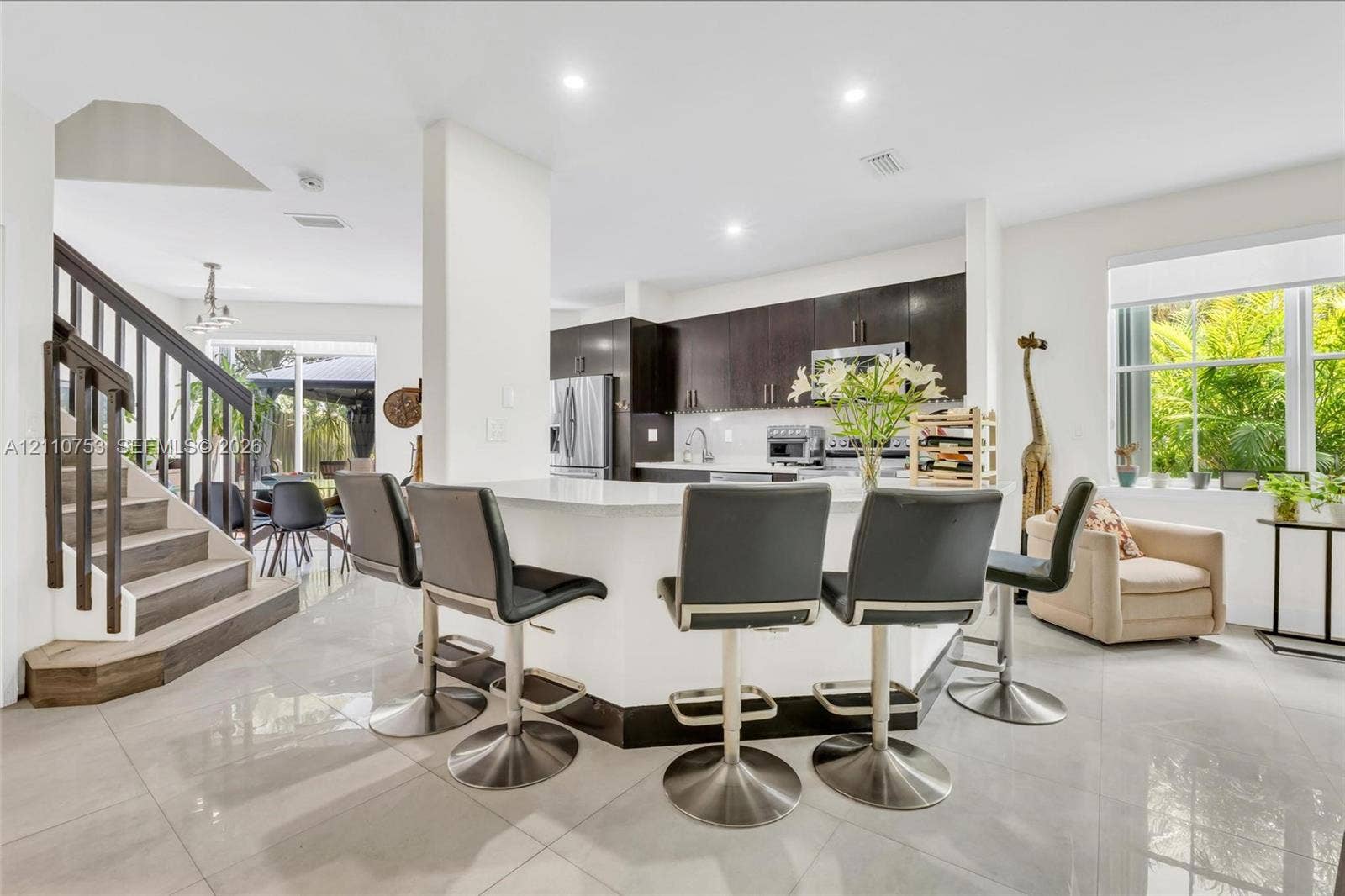 Kitchen featuring dark wood-finish cabinetry, white countertops, a wraparound peninsula, tiled flooring, and a staircase with metal balusters